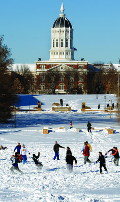 many people are playing in the snow near a building with a dome on it's roof