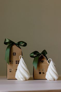 two small houses made out of cardboard with green ribbon on top and white icing on the outside