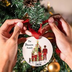 two hands holding a christmas ornament in front of a tree with ornaments on it