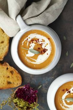 two bowls of carrot soup with bread on the side