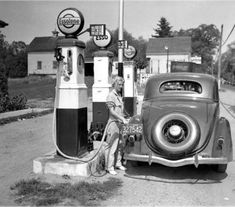 an old black and white photo of a woman at a gas station