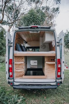 the back end of a white van with its doors open and wood shelves in it