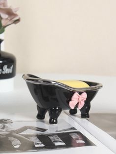 a black bowl with a pink bow sits on a table next to a photo and vase