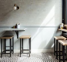 three wooden stools sit in front of a white wall with black and grey tiles