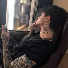 a man with tattoos sitting in a chair holding a cell phone and looking at the camera