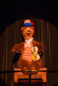 a large teddy bear sitting on top of a wooden chair with a violin in it's lap