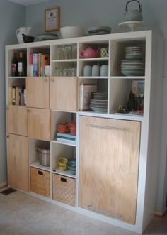 a white bookcase with lots of books and plates on it's shelves in a room