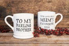 two coffee mugs sitting next to each other on top of a wooden table with berries