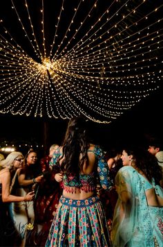 a group of people standing around each other in front of string lights and some trees