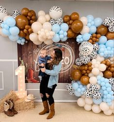 a woman holding a baby standing in front of a backdrop with balloons and other decorations