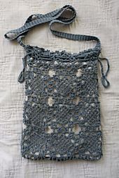 a gray crocheted bag sitting on top of a white tablecloth covered floor