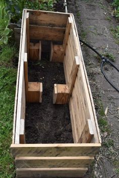 a wooden box filled with dirt next to a garden hose and some plants in it