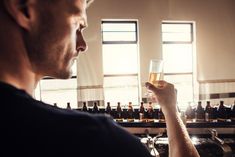 a man holding a glass in his right hand and looking at bottles on the other side