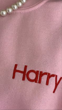 a pink sweater with the word harry written on it and pearls hanging down from the chest