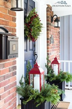 two red lanterns are sitting on the front porch with christmas wreaths and greenery