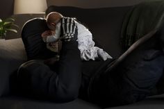 a baby sleeping on top of a black couch next to a green potted plant