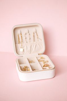 an open white box with jewelry in it on a pink surface, showing the contents inside