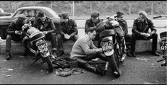 a group of men sitting on the side of a road next to parked motor cycles