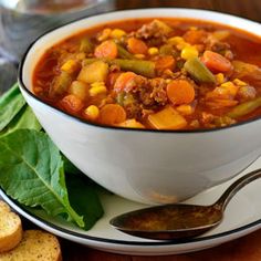 a white bowl filled with vegetable soup next to some bread on a plate and spoon