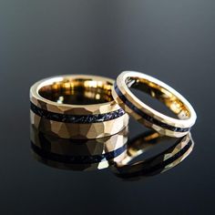 two wedding rings sitting on top of a black table next to each other and one has a diamond in the middle