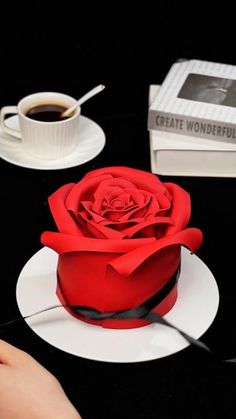 a red rose sitting on top of a white plate next to a cup of coffee