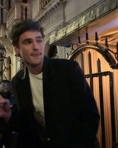 a man standing in front of a building holding a wine glass and looking at the camera