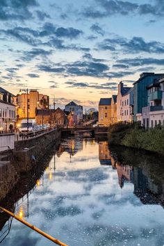 a river running through a small town with tall buildings on both sides and clouds in the sky