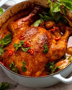 a pot filled with meat covered in sauce and garnished with green leaves on top