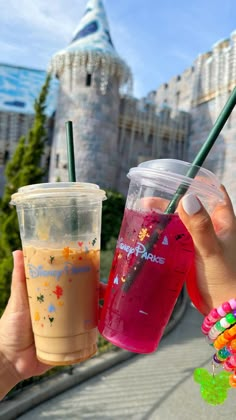 two people holding up drinks in front of a castle with the disney world logo on it