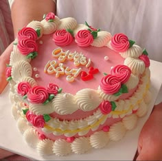 a pink and white birthday cake with roses on the top is being held by a person