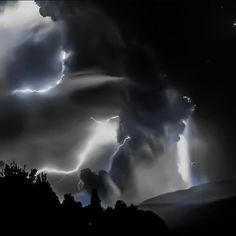 black and white photograph of storm clouds with lightning in the sky over trees at night