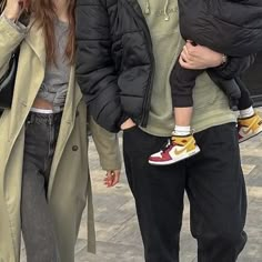 a man and woman walking down the street with a baby in their arms, both wearing sneakers