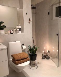 a white bathroom with candles and towels on the toilet seat, along with a potted plant