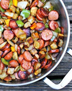 a pan filled with sausage and vegetables on top of a wooden table