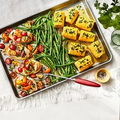 a tray filled with corn, green beans and tomatoes on top of a white table