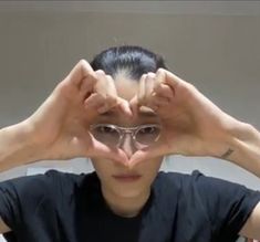 a man with glasses covering his eyes and making a heart shape