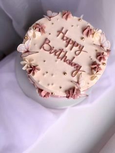 a birthday cake with pink frosting and butterflies on it sitting on a white table