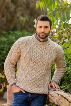 a man wearing a sweater and jeans leaning on a tree stump in front of some bushes