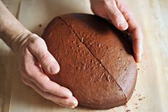 a person holding a large round cake on top of a wooden table next to a knife