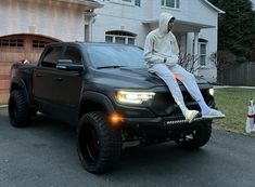 a man sitting on the hood of a black truck in front of a white house