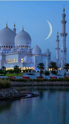 a large white building sitting next to a body of water at night with the moon in the sky