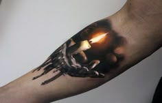 a man's arm is covered in black and grey ink with an image of a hand holding a lit candle