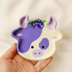 a hand holding a purple and white cow shaped object with green leaves on it's head