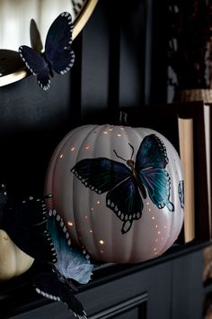 a white pumpkin with blue butterflies on it sitting on a mantle next to a book