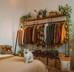 a white dog sitting on top of a bed next to a rack filled with clothes