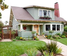 a green house with lots of plants in the front yard and landscaping on both sides