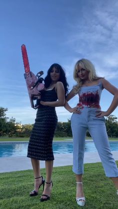 two women standing next to each other in front of a pool holding chainsaws