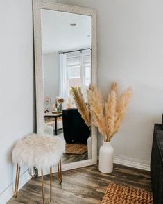 a mirror sitting on top of a wooden floor next to a white vase filled with flowers