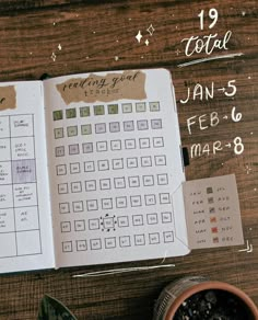 an open planner sitting on top of a wooden table next to a potted plant