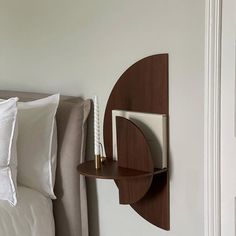 a bed with white pillows and a wooden shelf on the wall next to its headboard